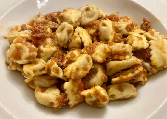 Small folded pasta parcels with pinched edges and a coarse brown meat sauce on a white plate