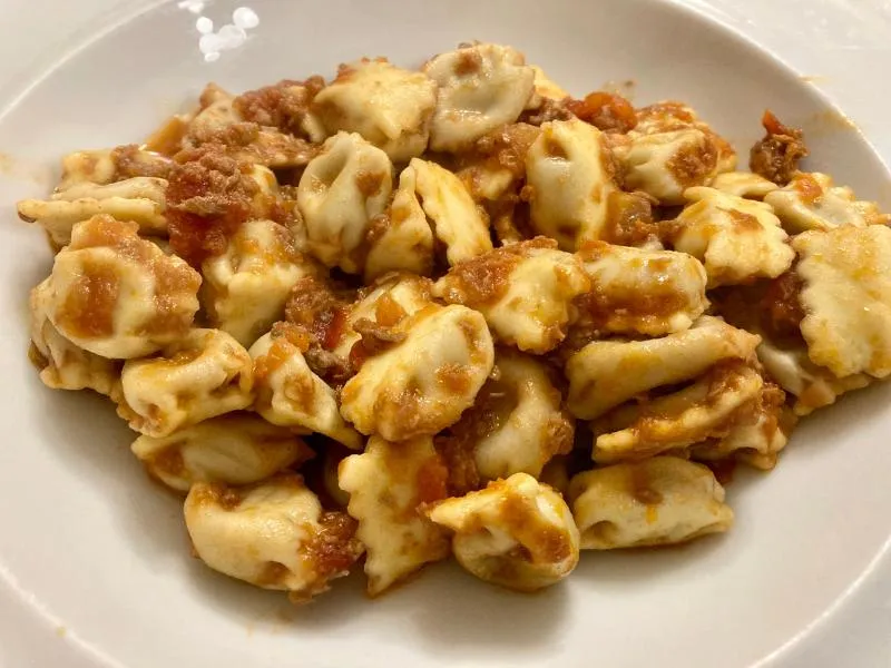 Small folded pasta parcels with pinched edges and a coarse brown meat sauce on a white plate