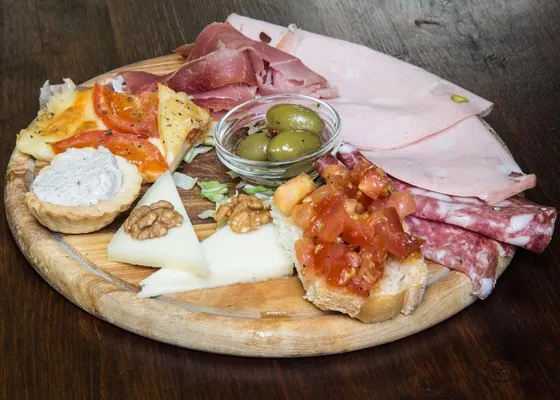 A wooden board of sliced cured meats, cheese, olives, tomato crostini and other small prepared bites