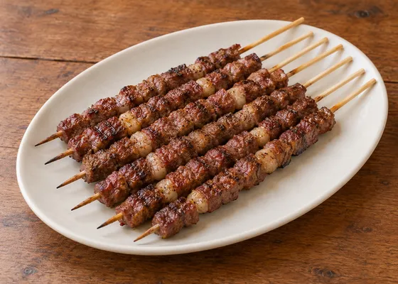 Slender skewers threaded with small browned sheep-meat and fat cubes, arranged on a white oval plate