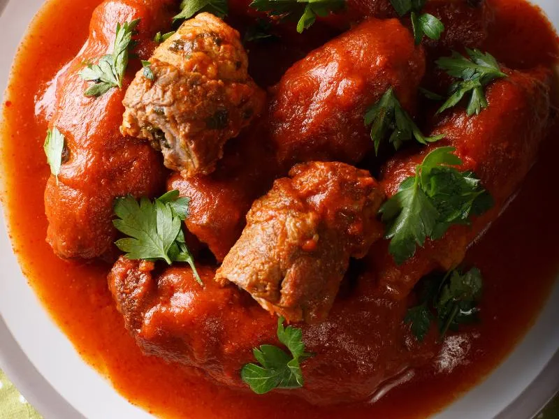Stuffed beef rolls in red tomato sauce, with one cut open and parsley leaves scattered over the plate