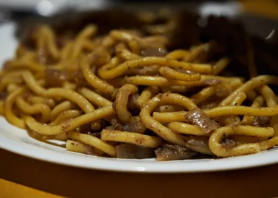 Thick pasta strands coated in a brown onion sauce with visible pieces of softened onion on a white plate