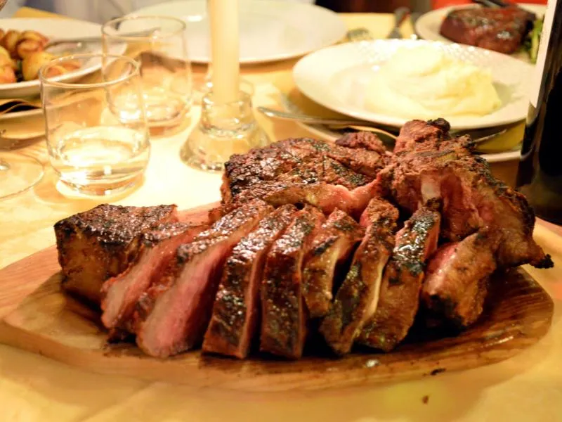 A thick grilled T-bone steak with a browned crust, served on a board