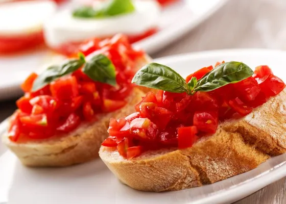 Thick slices of toasted bread topped with chopped red tomatoes and fresh basil leaves on a white plate