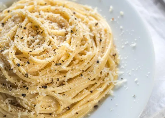 Spaghetti with grated cheese and cracked black pepper on a white plate