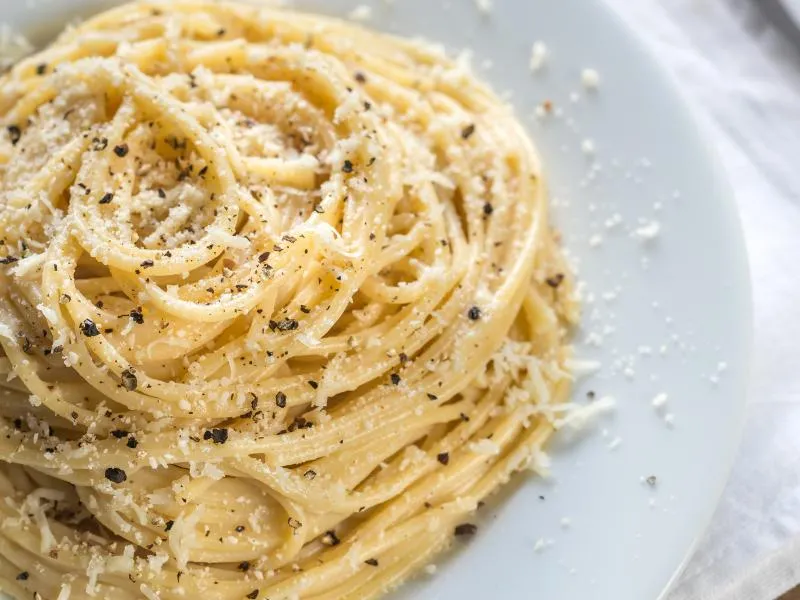 Spaghetti with grated cheese and cracked black pepper on a white plate