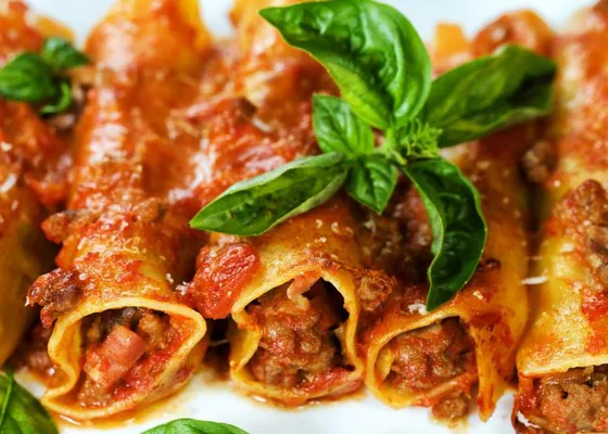 Meat-filled pasta rolls with red tomato sauce, grated cheese and broad basil leaves on a white plate