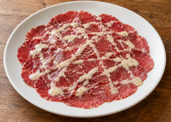 Paper-thin slices of raw red beef with a pale mayonnaise-based sauce on a white plate
