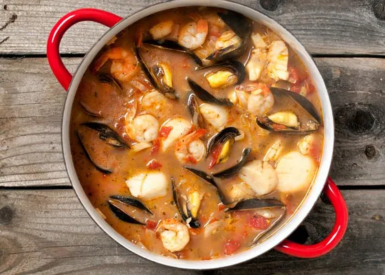 A red pot of tomato seafood stew with mussels, shrimp and white fish