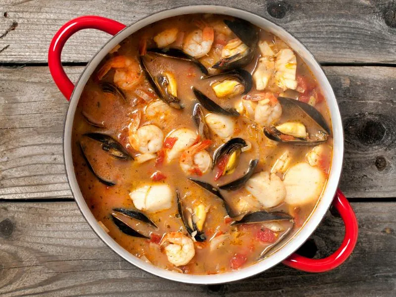 A red pot of tomato seafood stew with mussels, shrimp and white fish