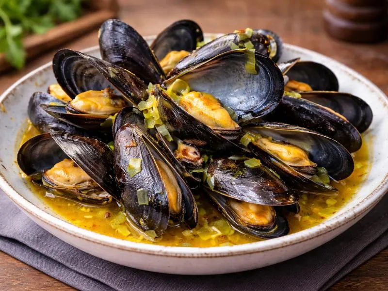Opened mussels piled in a shallow bowl with golden saffron broth and small pieces of softened leek
