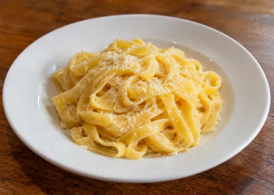 Golden fettuccine ribbons with a glossy butter-and-cheese coating and grated Parmigiano on a white plate
