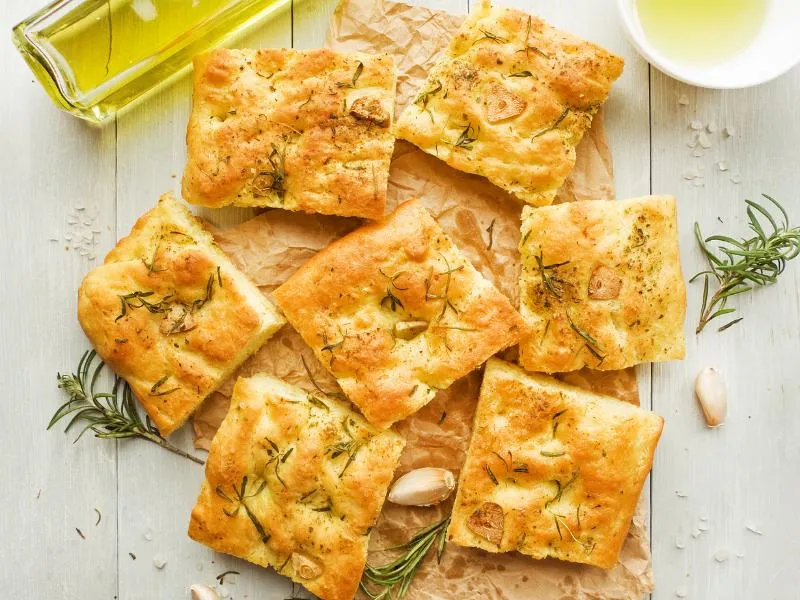 Squares of golden dimpled focaccia with rosemary on a board
