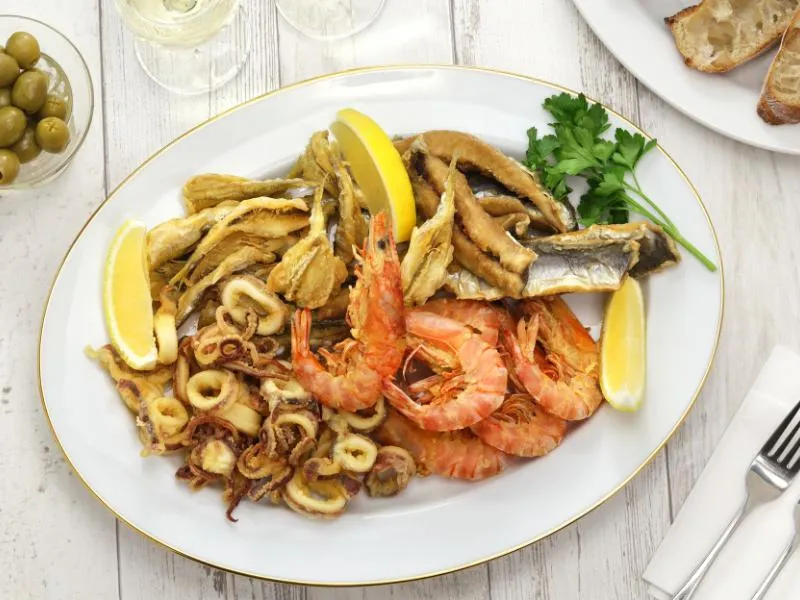 A platter of fried squid rings, shell-on shrimp and small fish with lemon wedges and parsley