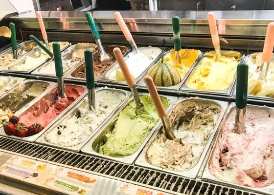A gelateria display of metal tubs containing several colors and flavors of gelato, with serving paddles