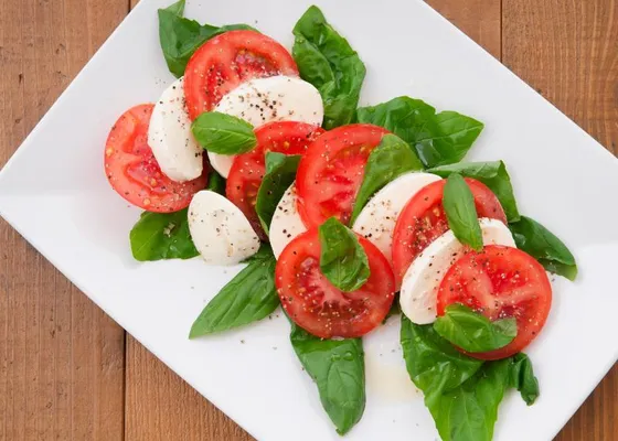 Alternating tomato and mozzarella slices with basil leaves on a white plate