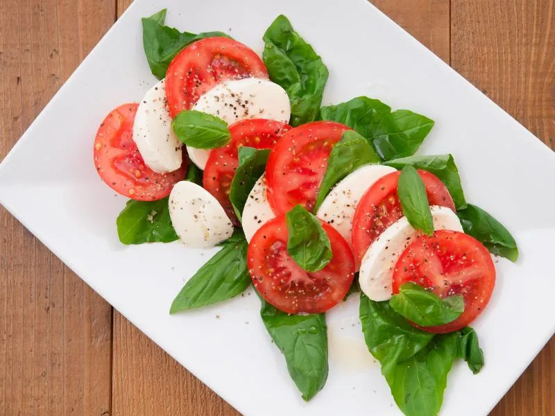 Alternating tomato and mozzarella slices with basil leaves on a white plate