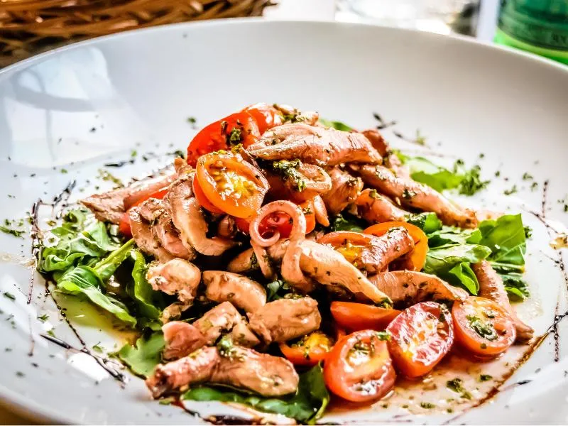 Pieces of octopus with cherry tomatoes, leafy greens and chopped herbs on a white plate