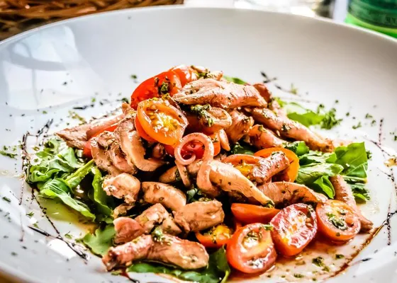 Pieces of octopus with cherry tomatoes, leafy greens and chopped herbs on a white plate