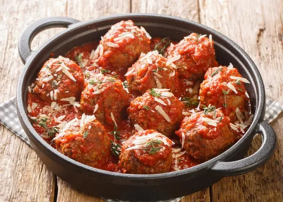 Large round meatballs in thick red tomato sauce with grated cheese and green herbs in a black handled pan