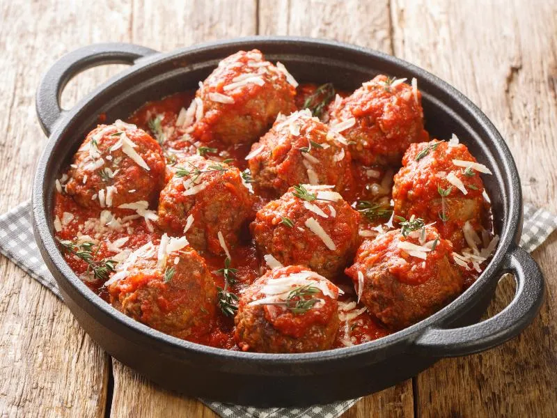 Large round meatballs in thick red tomato sauce with grated cheese and green herbs in a black handled pan