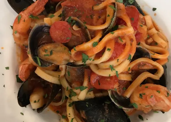 Long flat pasta with mussels, shrimp, tomato pieces and chopped parsley on a white plate