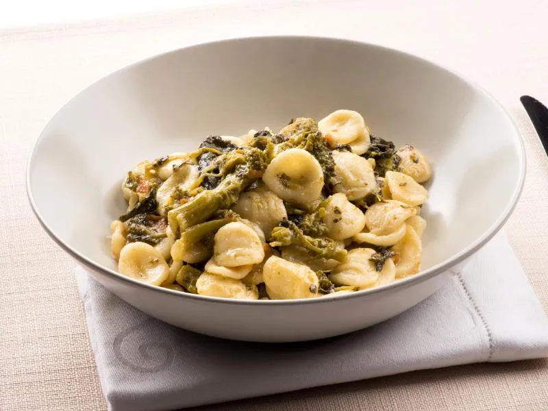 Orecchiette pasta mixed with dark leafy greens in a white bowl