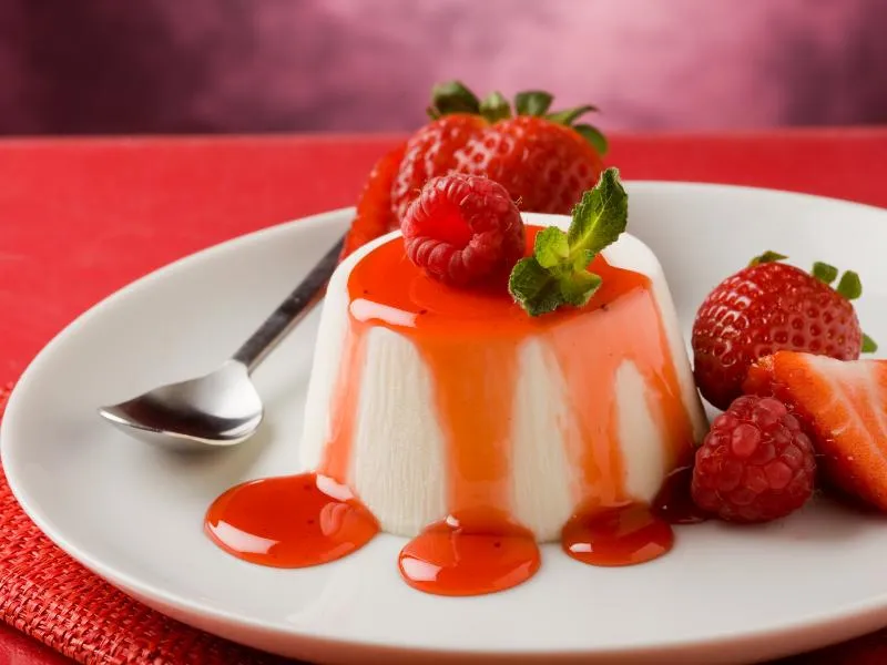 Unmolded panna cotta with red berry sauce and fresh berries