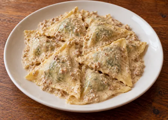 Triangular handmade pasta parcels coated in pale textured walnut sauce on a white plate