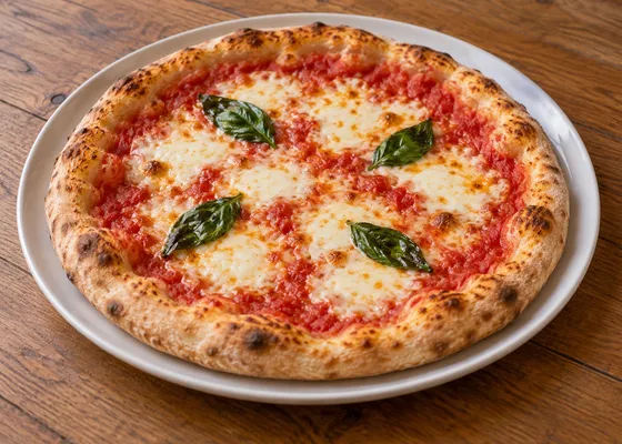 A whole round Margherita pizza with tomato, melted mozzarella, basil and a browned raised crust on a white plate