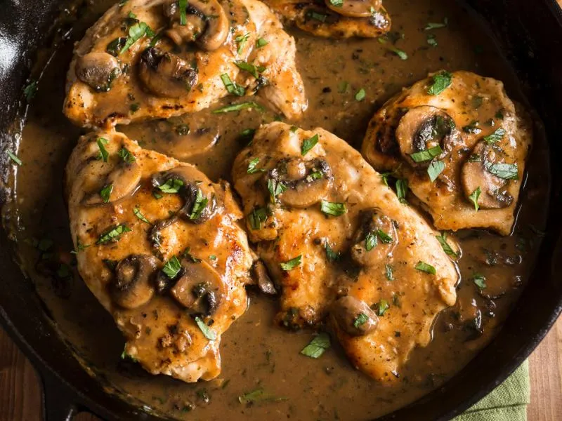 Chicken cutlets with sliced mushrooms in a brown sauce, topped with parsley in a skillet