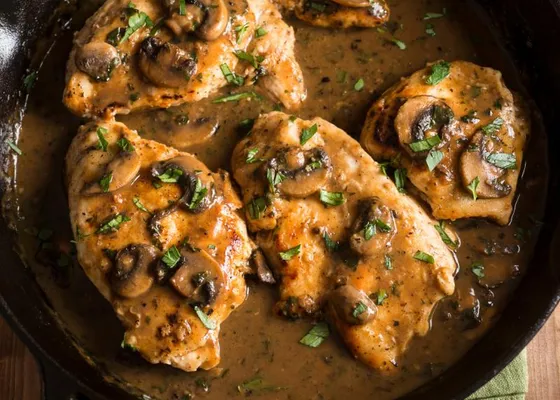 Chicken cutlets with sliced mushrooms in a brown sauce, topped with parsley in a skillet