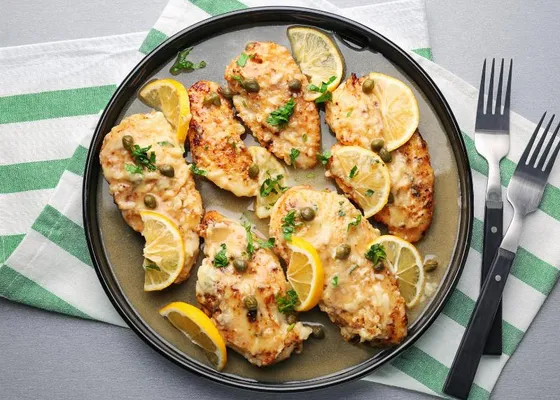 Golden chicken cutlets topped with capers, lemon slices and chopped parsley on a dark plate