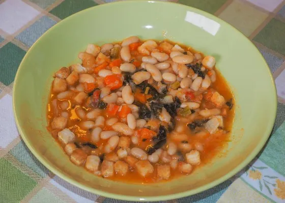 A rustic bowl of bean and vegetable soup with carrots and dark greens
