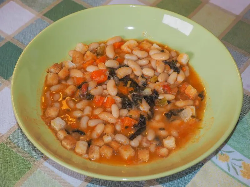 A rustic bowl of bean and vegetable soup with carrots and dark greens
