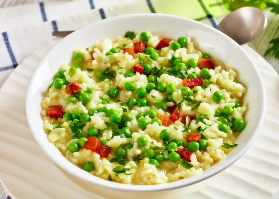 Rice and green peas in a white bowl with browned pancetta cubes, grated cheese and chopped parsley