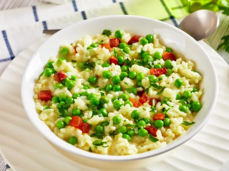 Rice and green peas in a white bowl with browned pancetta cubes, grated cheese and chopped parsley