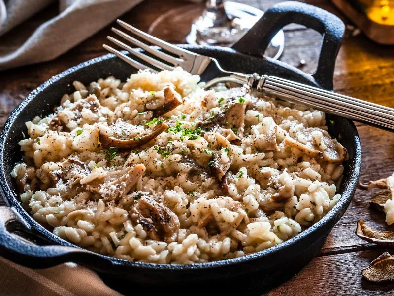 Creamy rice topped with sliced mushrooms, grated cheese and chopped herbs in a black handled pan