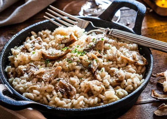 Creamy rice topped with sliced mushrooms, grated cheese and chopped herbs in a black handled pan