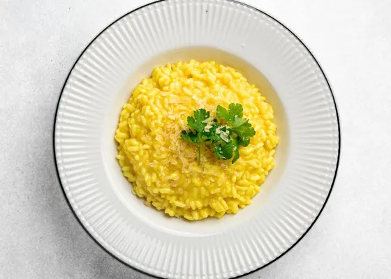 Golden saffron risotto on a white plate with a small green herb garnish