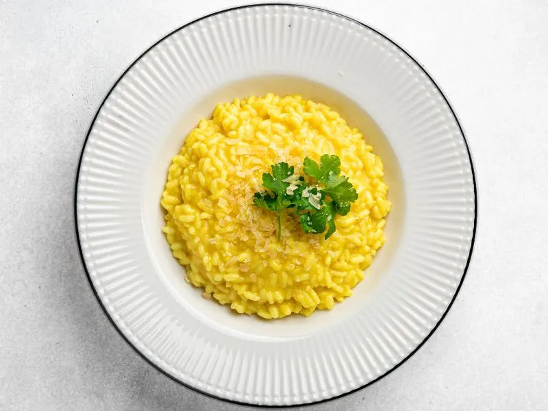 Golden saffron risotto on a white plate with a small green herb garnish