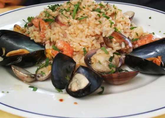 Seafood risotto with mussels and clams in their shells, shrimp and chopped parsley on a white plate