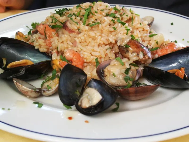 Seafood risotto with mussels and clams in their shells, shrimp and chopped parsley on a white plate