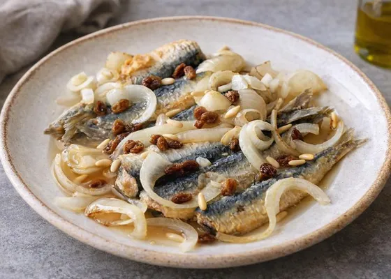 Opened sardine fillets layered with pale onion rings, raisins and pine nuts on a ceramic plate