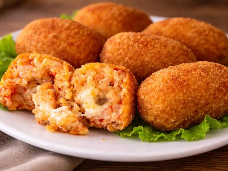 Golden oblong rice croquettes, one cut open to show tomato rice and mozzarella