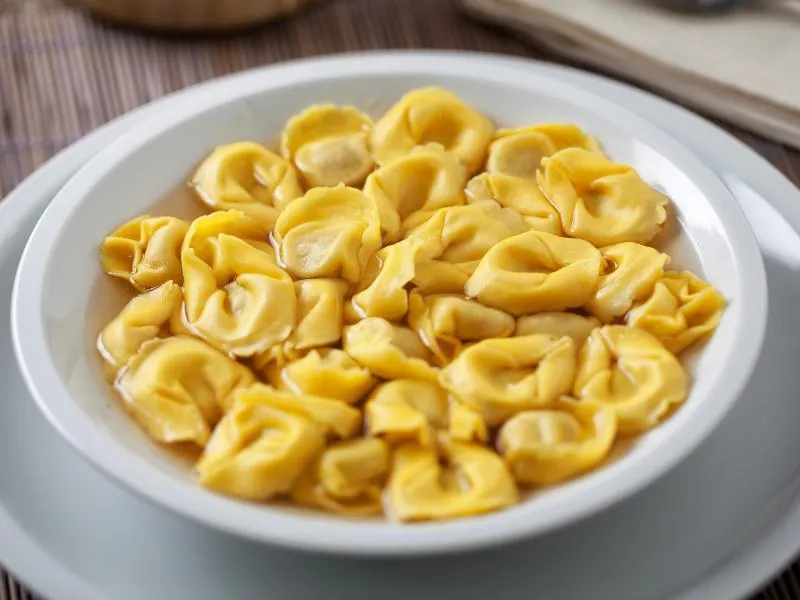 Small yellow ring-shaped filled pasta in pale golden broth in a deep white bowl