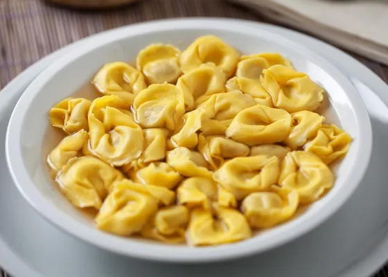 Small yellow ring-shaped filled pasta in pale golden broth in a deep white bowl