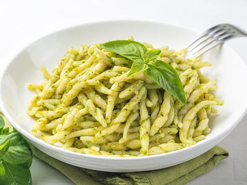 Short twisted pasta coated in green pesto with basil leaves on top
