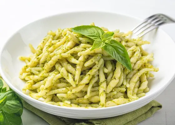 Short twisted pasta coated in green pesto with basil leaves on top
