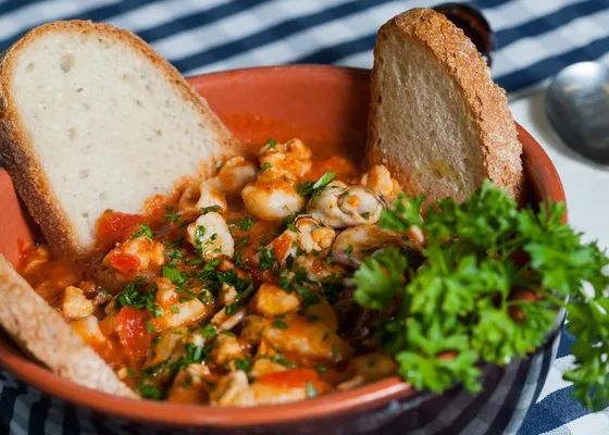 Pieces of fish and shellfish in a red tomato broth, with toasted bread and parsley in a terracotta bowl